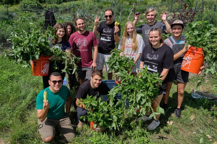 Students stand in the garden, smiling with their plants. 