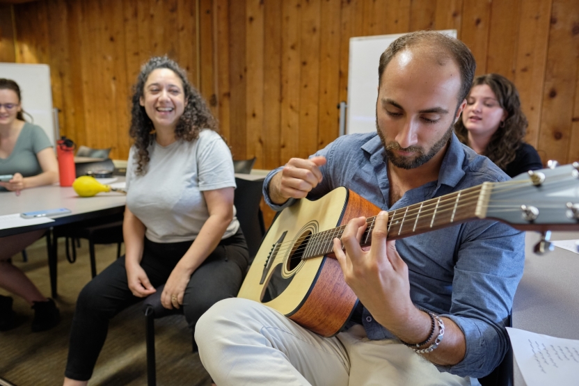 A man plays guitar and a woman smiles behind him.