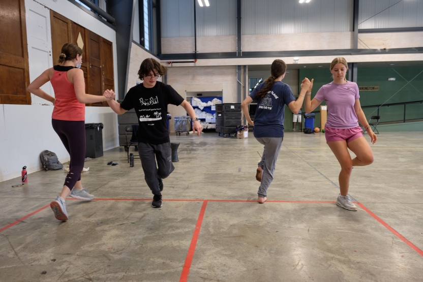 Students perform a dance, holding hands. 