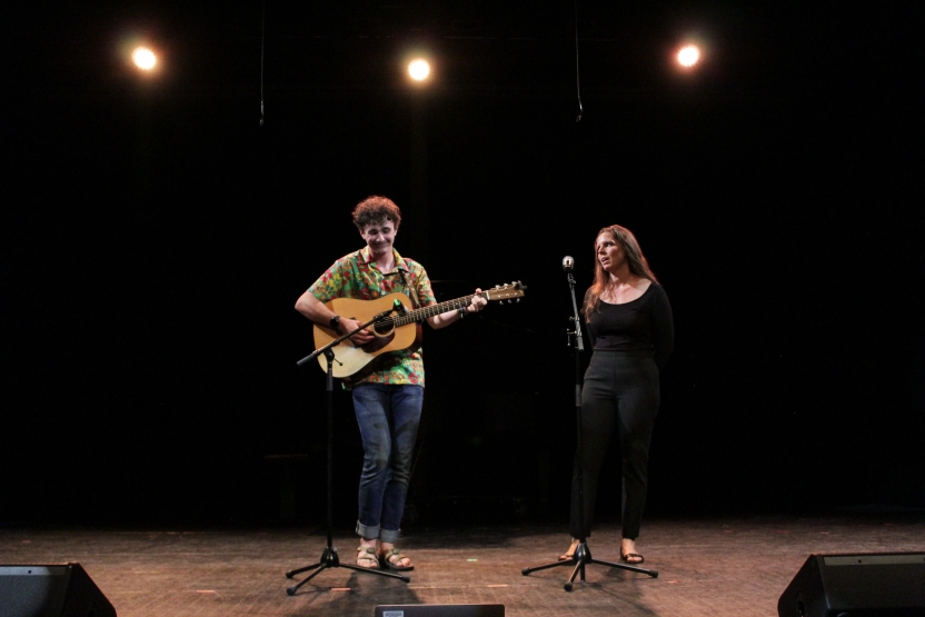 One person plays guitar and another sings onstage. 