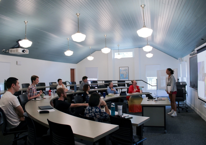 Students sit in a large, airy classroom. 
