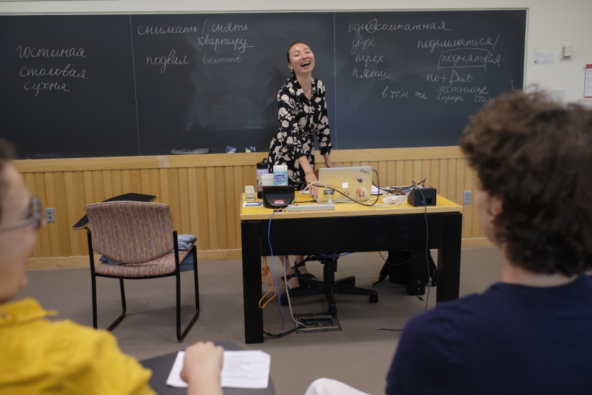 A teacher laughs at a blackboard with Russian writing on it. 