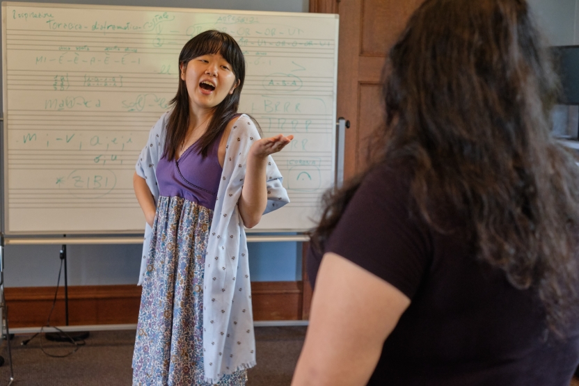 A student gestures as she sings in front of a whiteboard. 