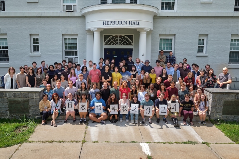 A group of students at the School of Japanese smiles at the camera in front of Hepburn Hall at Middlebury College. 