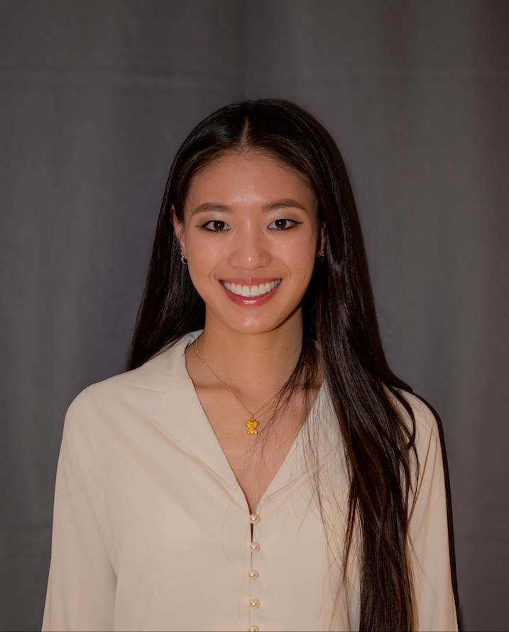 A woman with long black hair in a white shirt and gold necklace smiles at the camera.