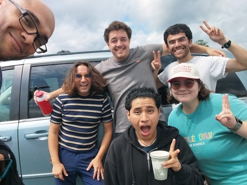 A group of students smiles at the camera in front of a gray van.