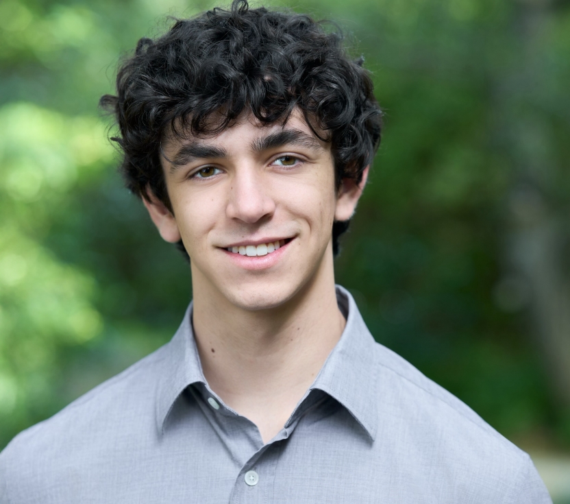 A man in a gray collared shirt smiles at the camera.