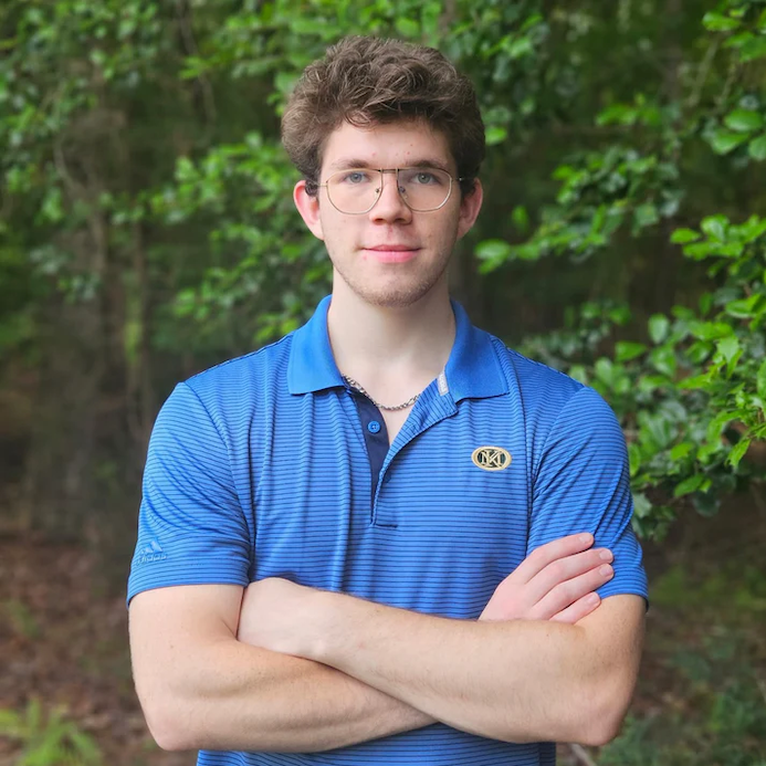 A man in a blue short sleeved collar shirt looks at the camera.