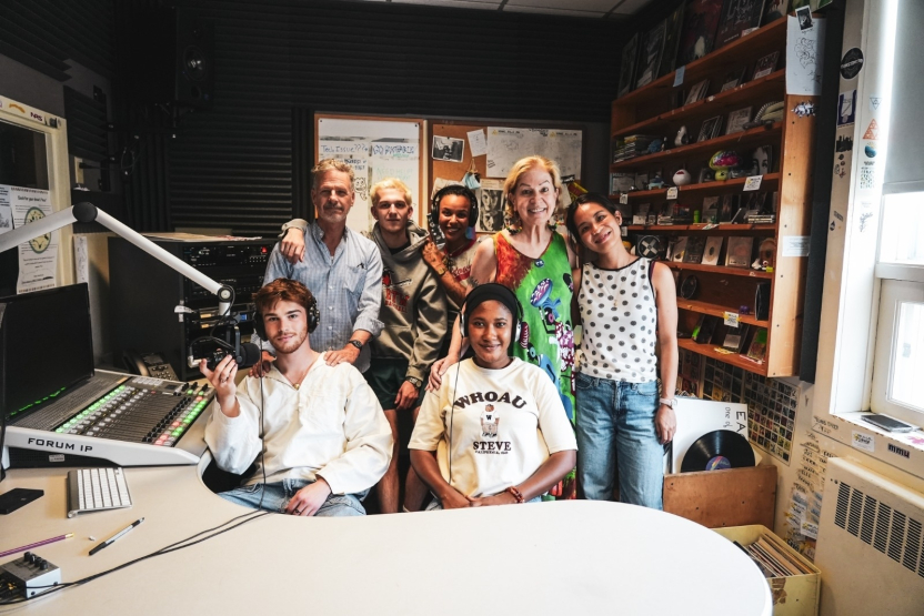 A woman stands with a group in a recording studio. 