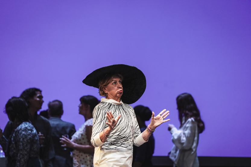 a woman performs onstage in a large hat. 