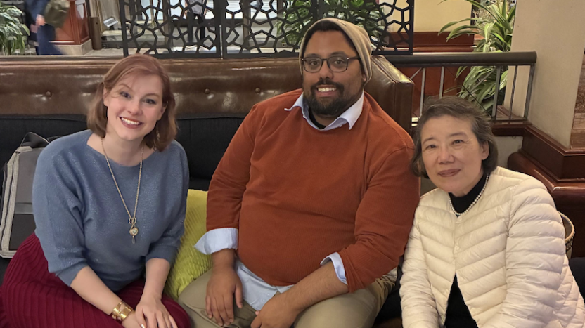 A man in a red sweater poses with School of Korean director Sahie Kang and a fellow School of Korean alum