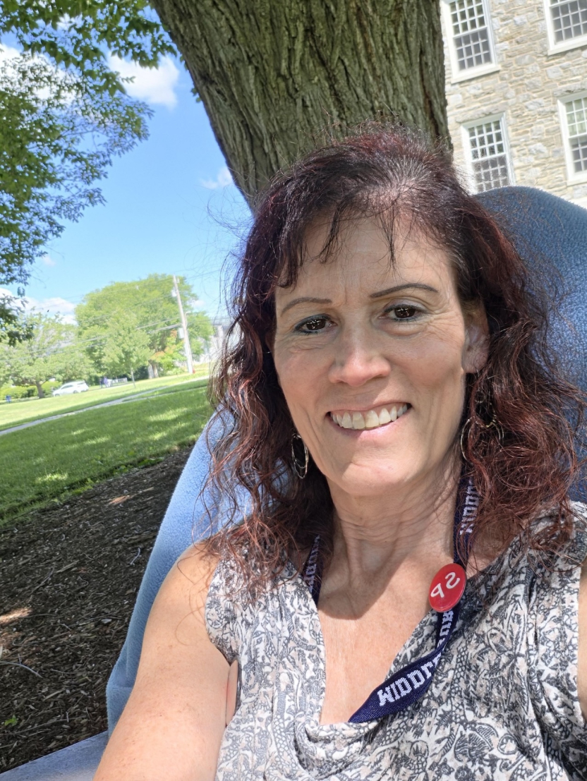 Woman with Red School of Spanish pin in an Adirondack chair smiling at the camera