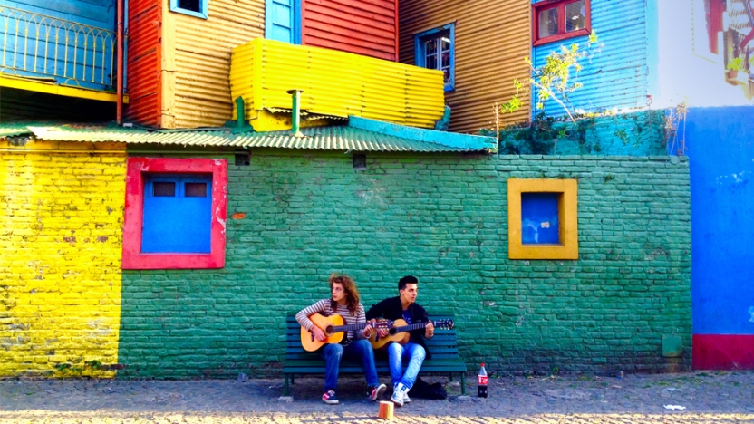Two students sitting on a bench playing guitars.