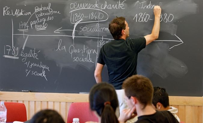 A professor writes French on the chalk board.