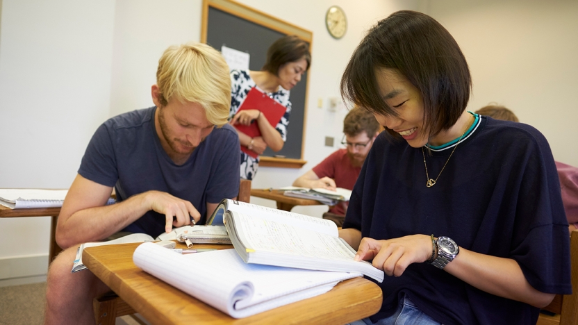 A male and female student work together over a textbook in a classroom setting.