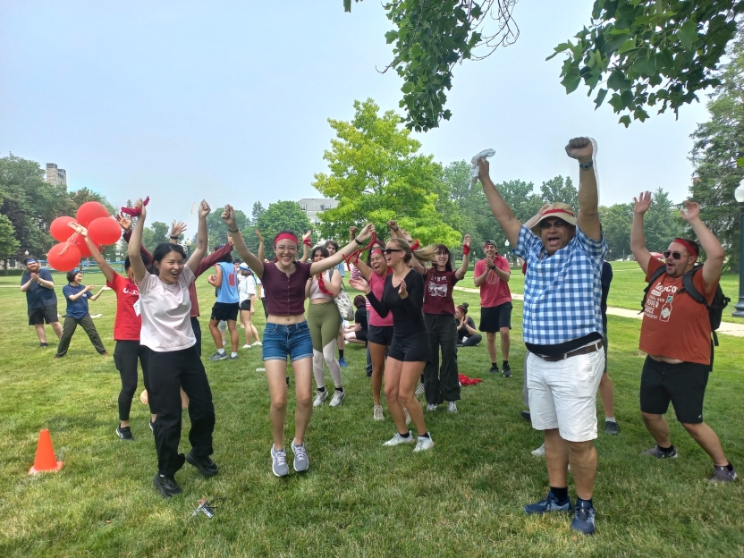 A group of students in color coordinated team gear jumps for joy.