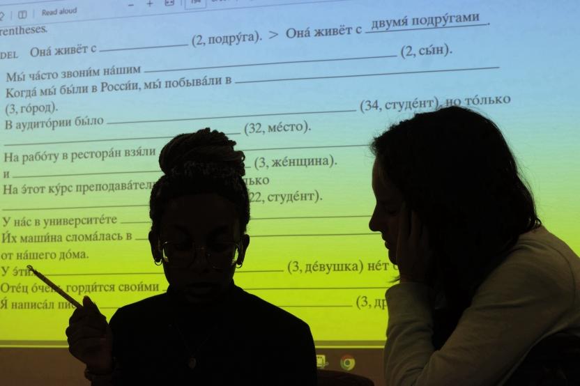 Students sit in front of a screen with Russian writing. 