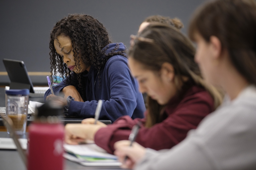 A woman takes notes in class alongside her two classmates.