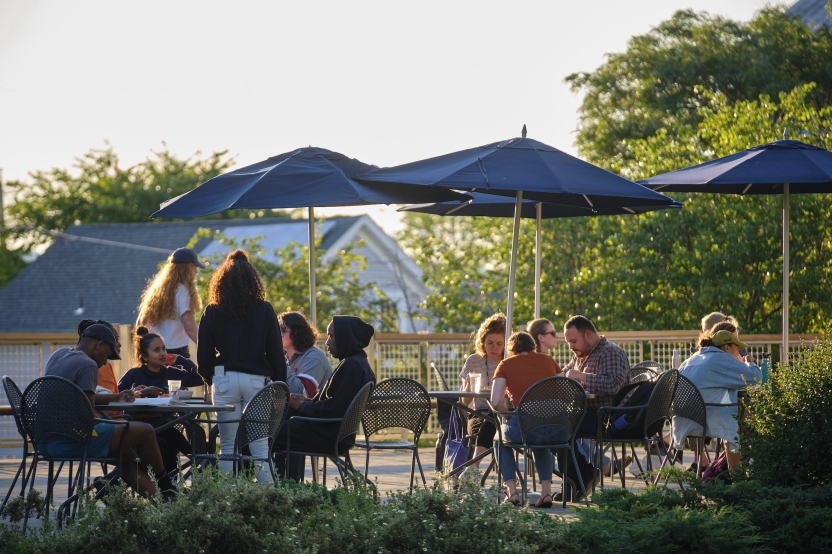 Students dine outdoors under umbrellas at golden hour. 