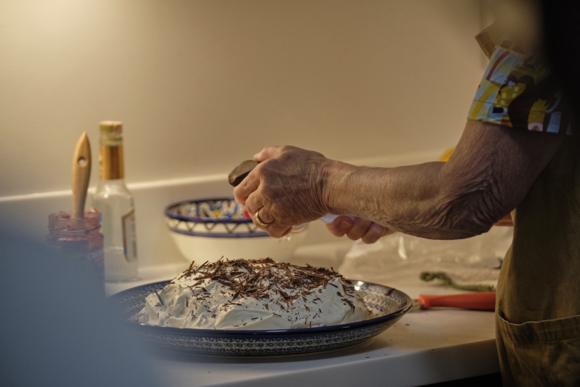 A woman grates chocolate over a frosted cake/pie. 