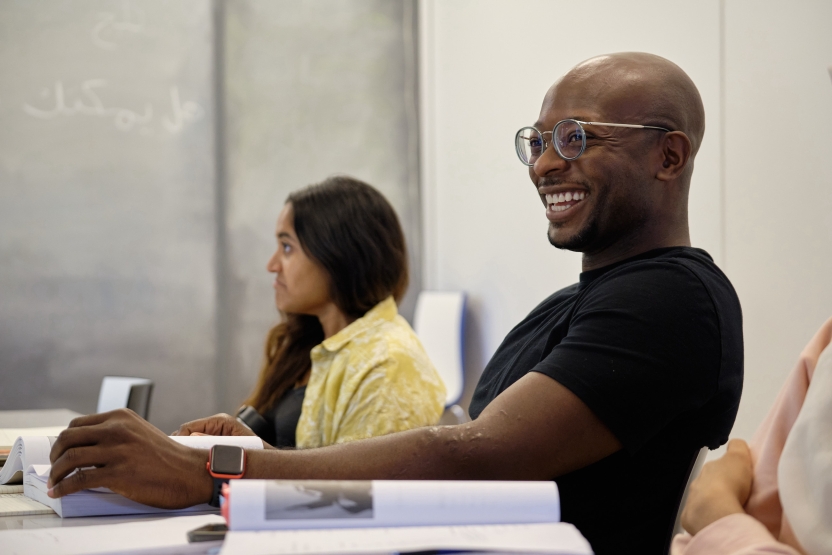 A student smiles as he participates in class seated at his desk.