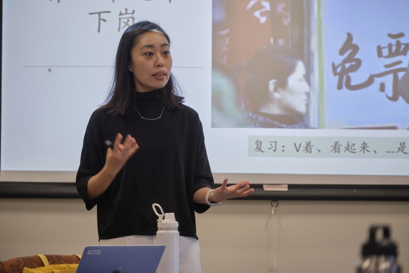 A teacher stands at the board in front of Chinese characters. 