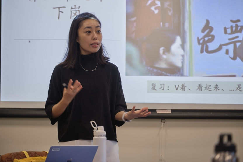 A teacher stands at the board in front of Chinese characters.