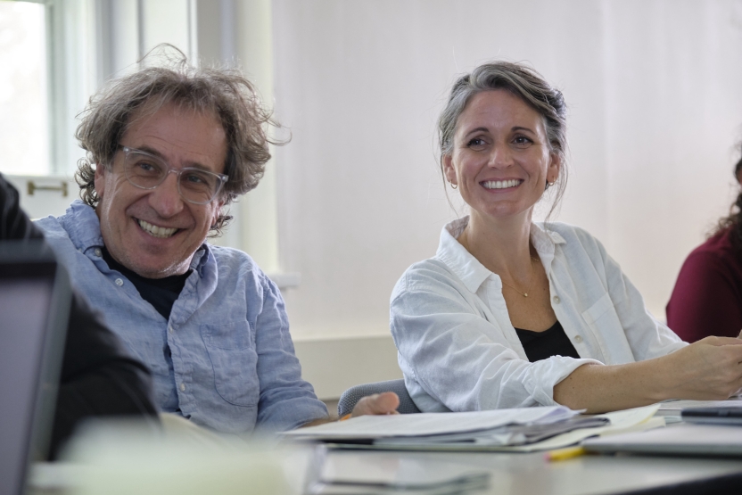 Two students sit side by side in class, smiling up at the teacher.