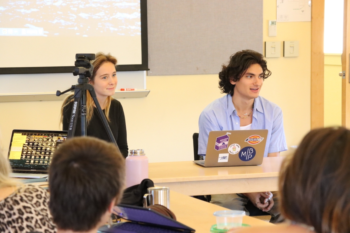 Two students sit in front of a computer facing an audience