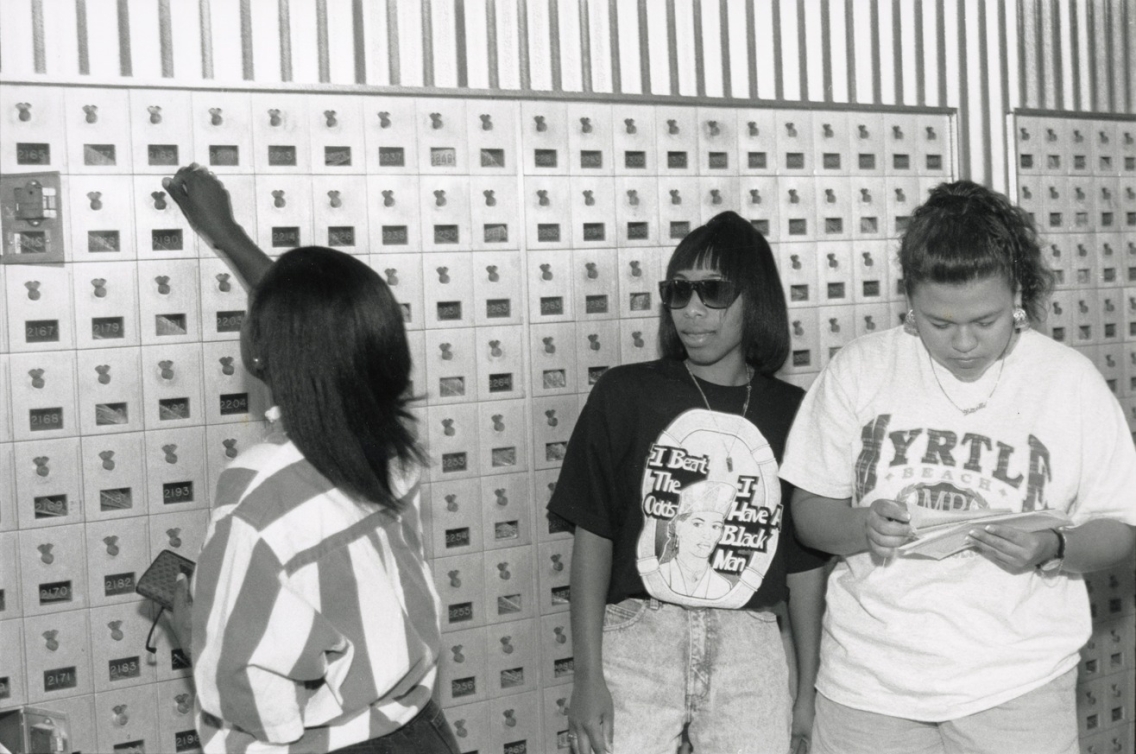 Black and white photograph of three female students of color in front of the student mailboxes at Middlebury College.