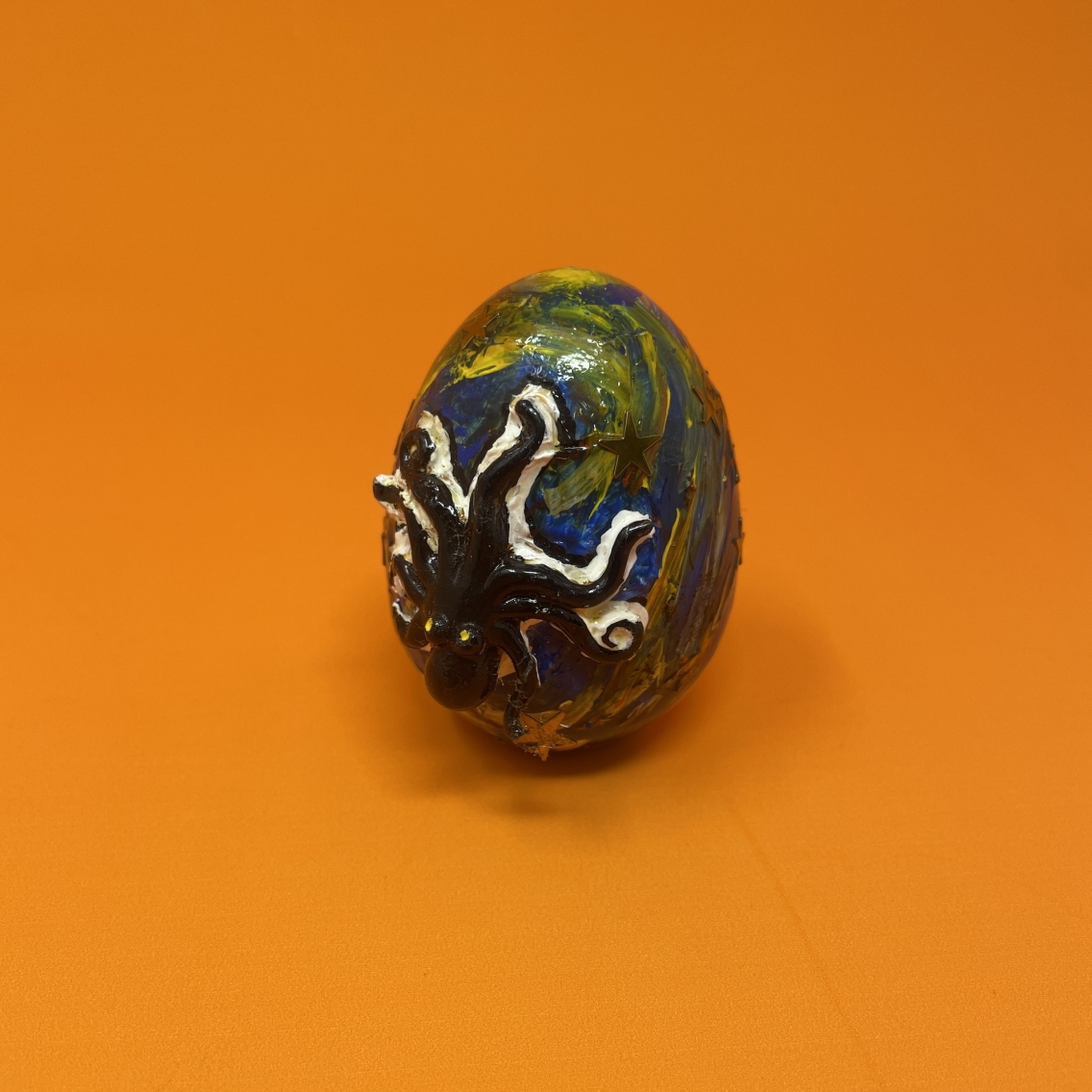 Painted egg with black octopus outlined in white against orange background