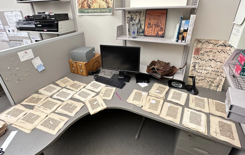 stacks of manuscript Quran pages on an L-shaped work desk
