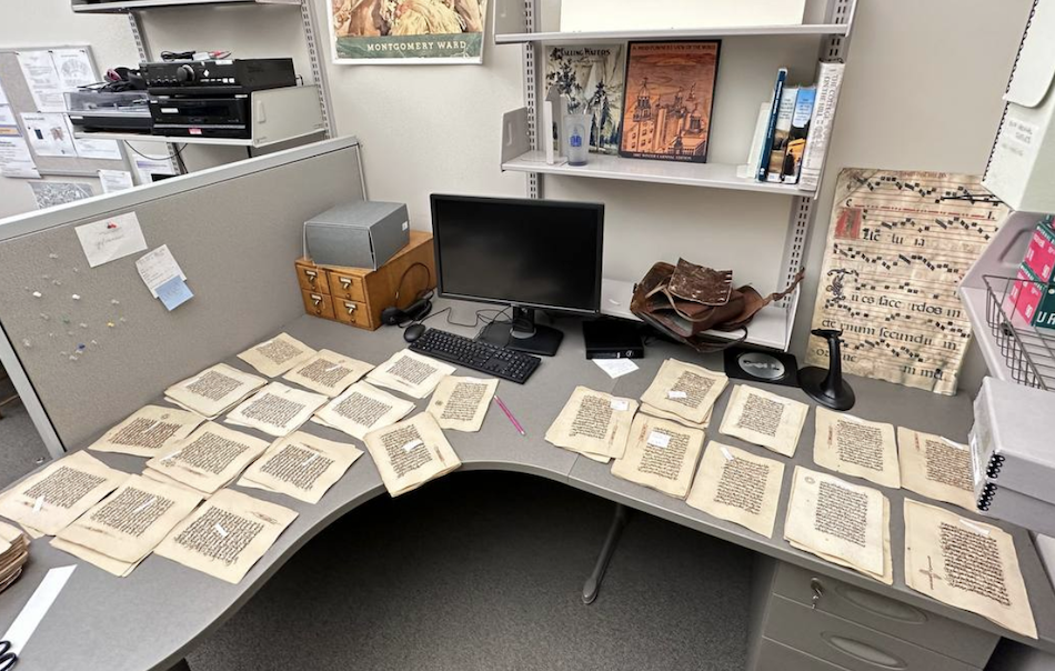 stacks of manuscript Quran pages on an L-shaped work desk 