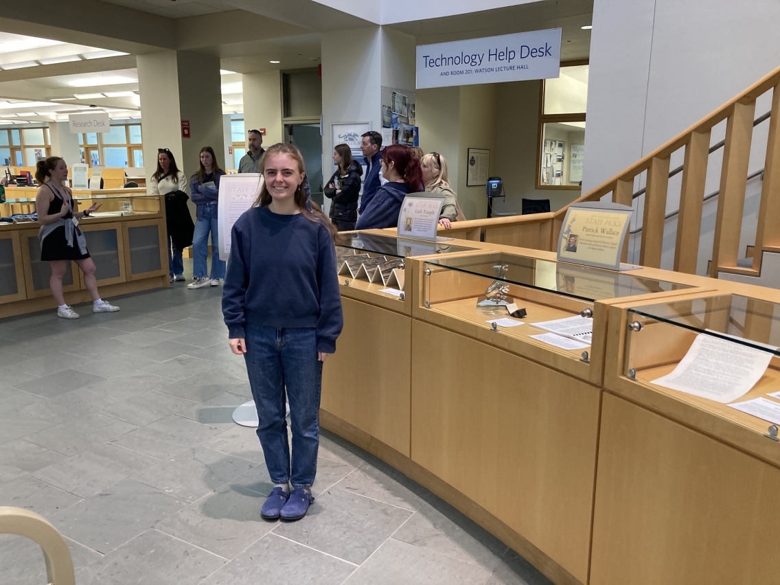 student standing in front of library exhibition showcases with group of people in background