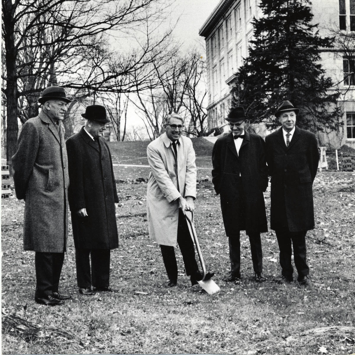 group of men in hats, coats, and ties with center man holding a shovel