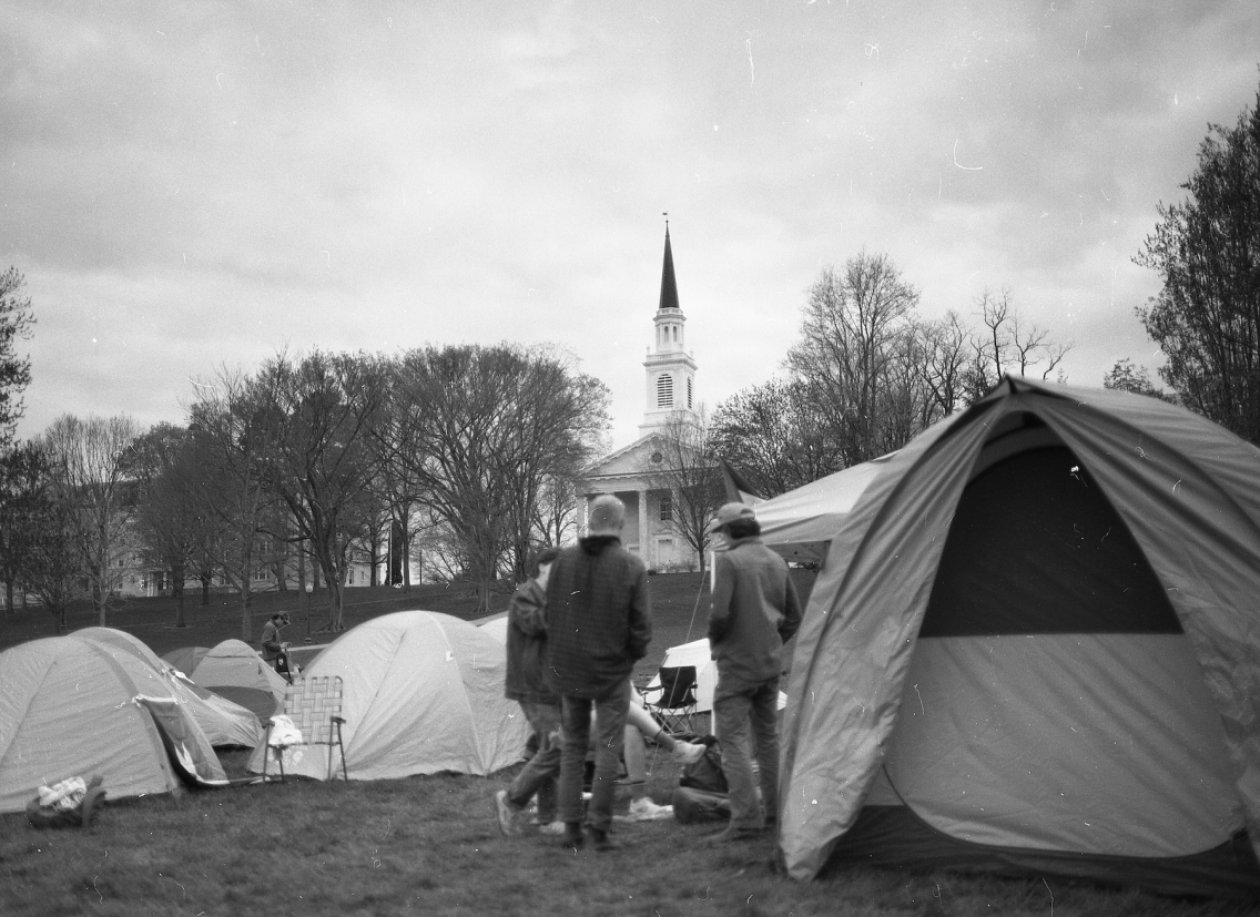 black and white photo of tents, a group of people on lawn with Middlebury Chapel in background