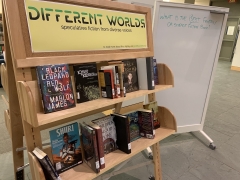 a picture of books on a book display cart labelled "Different Worlds: speculative fiction from diverse voices"