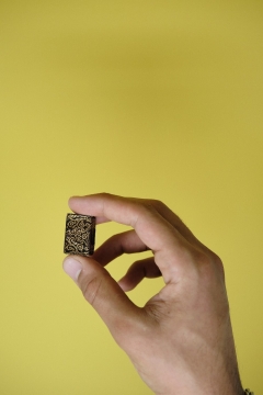 Hand holds miniature brown and gold Qur'an against yellow background