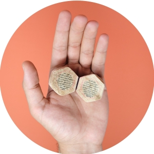 Photograph of hand holding tiny Qur'an against a red background.