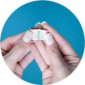 Hands holding a miniature book against a blue background