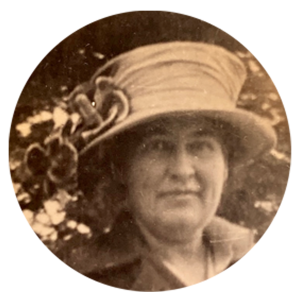 headshot of woman wearing brimmed hat with flowers in front of a tree