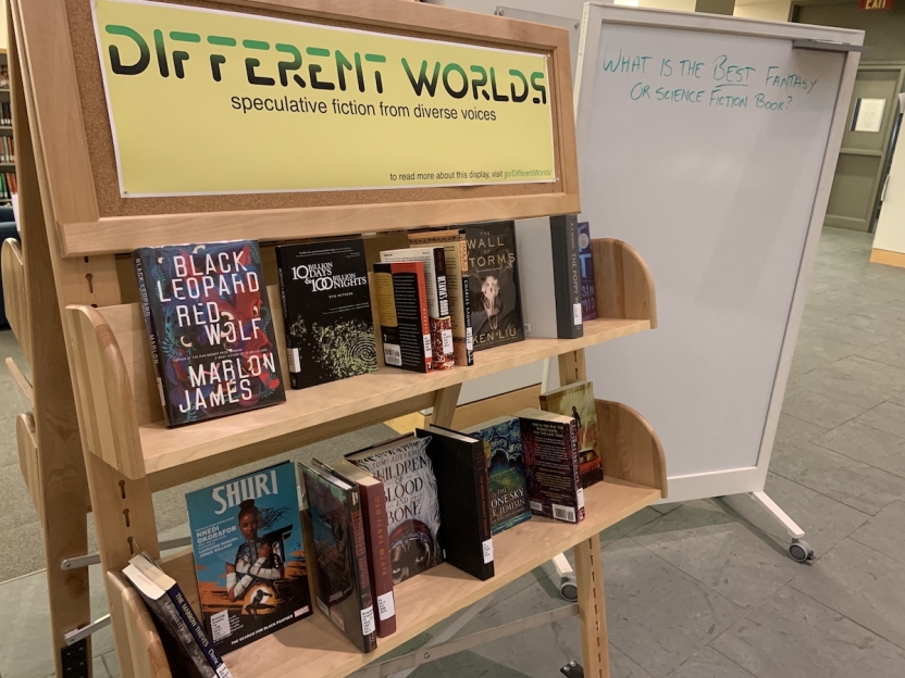 a picture of books on a book display cart labelled "Different Worlds: speculative fiction from diverse voices"