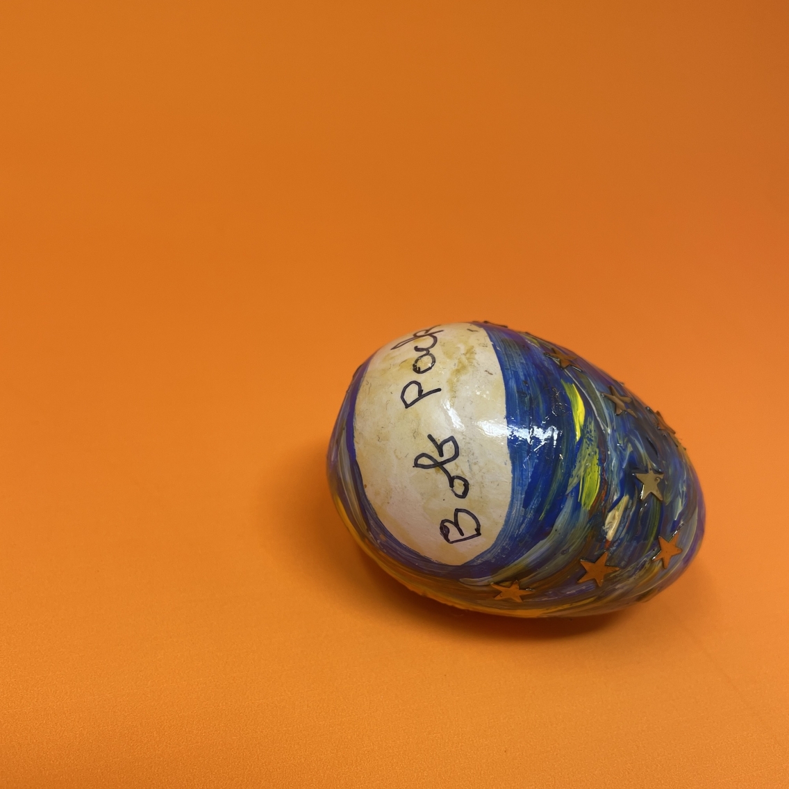 Painted wooden egg with the name "Bob Pack" signed, against orange background