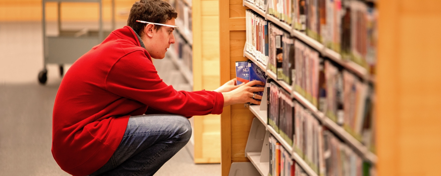 Male student pulling book off shelf in library.