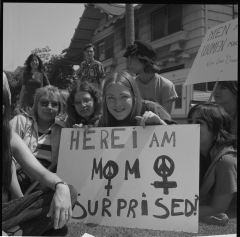 women sitting on a lawn with the sign "here I am mom, surprised?"