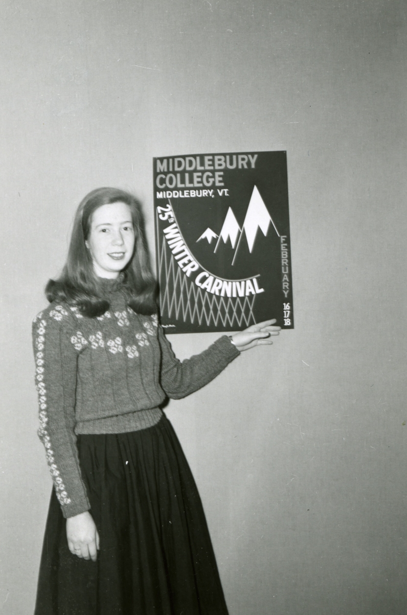 Marylin Martin ’59, winner of 1956 Winter Carnival poster design contest, poses in front of winning poster hanging on a wall