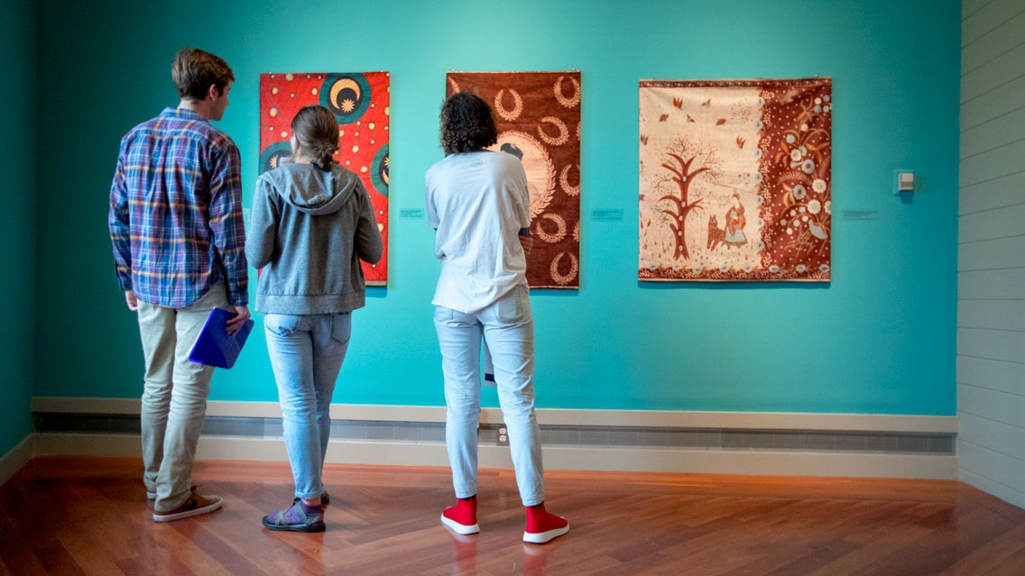 Students viewing three art pieces at the Middlebury Museum.