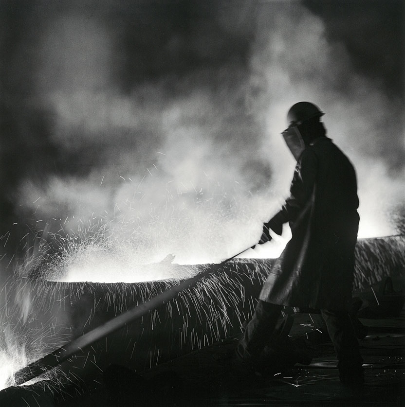 man working in a steel mill with molten steel in vats in front of him