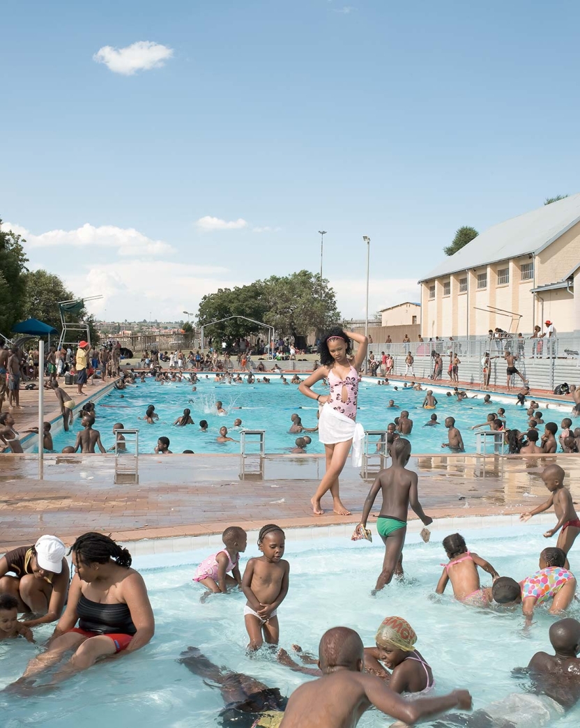 hundreds of people, mostly children, enjoy the shallow waters of a large community swimming pool