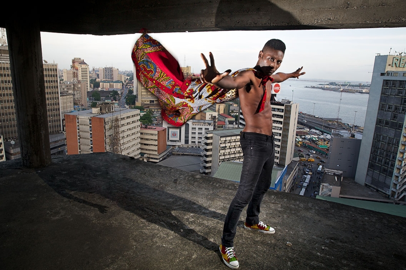 Captain Rugged stands above the city skyline with arms outstretched and brightly colored cape flowing in the wind